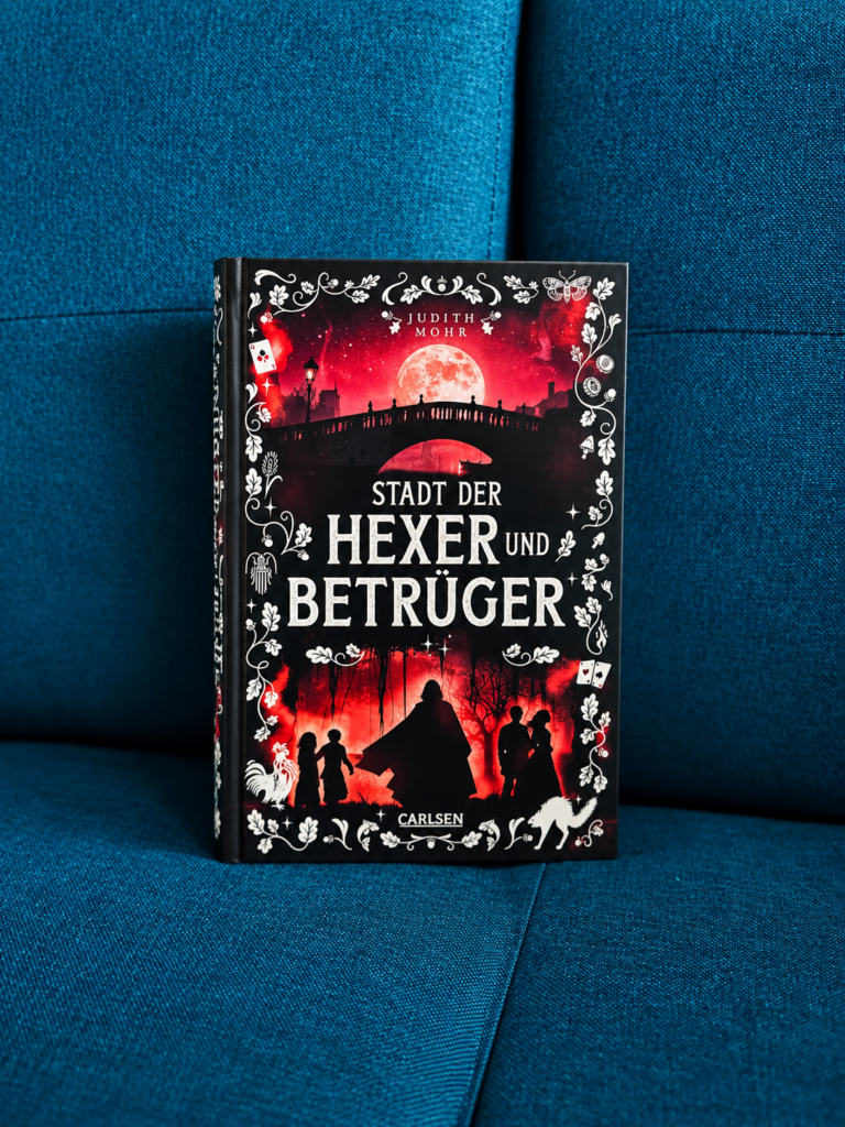 Fantasy-Jugendbuch „Stadt der Hexer und Betrüger“ von Judith Mohr aus dem Carlsen Verlag auf einer mintgrünen Decke in einem gemütlichen Teenagerzimmer als perfekte Urlaubslektüre.